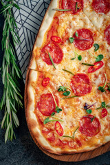 Spicy long pepperoni pizza with sausage and pepper. Italian extra-size pizza served on a wooden board, close-up