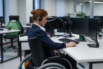 Red-haired caucasian woman in a wheelchair talking on a headset. Female call center worker at her desk.