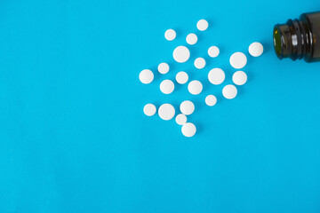 Scattered medicine white pills and glass container at blue background with copy space