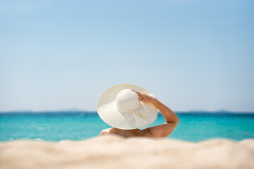 A woman in a white hat sits in the sand against the background of the sea
