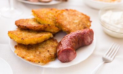 Potato pancakes with fried sausage on white plate
