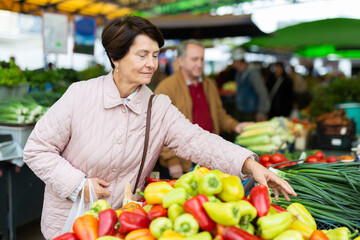 Aged woman customer buying pepper in open-air market