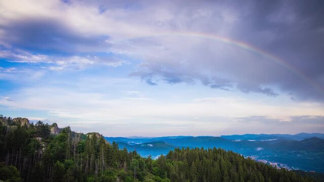 Multi-colored rainbow flaunts on top of the Rhodope Mountains above intermountain valley with the village of Smolyan