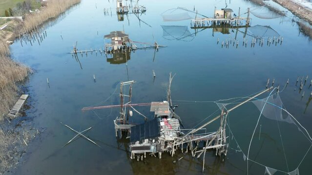 Traditional fishing huts on the river - old-style cabins with raised torn nets on wooden pillars over the Port Milena water canal or lake near Ulcinj Montenegro. Aerial drone view.