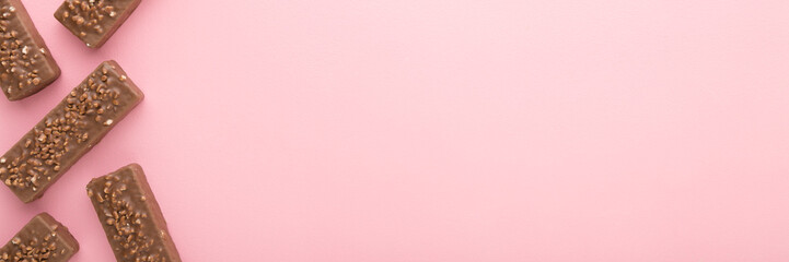 Dark brown chocolate bars with nuts on light pink table background. Pastel color. Sweet snack. Closeup. Empty place for text. Wide banner. Top down view.