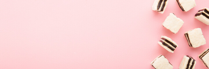 White jelly gummy candies with dark chocolate on light pink table background. Pastel color. Sweet...