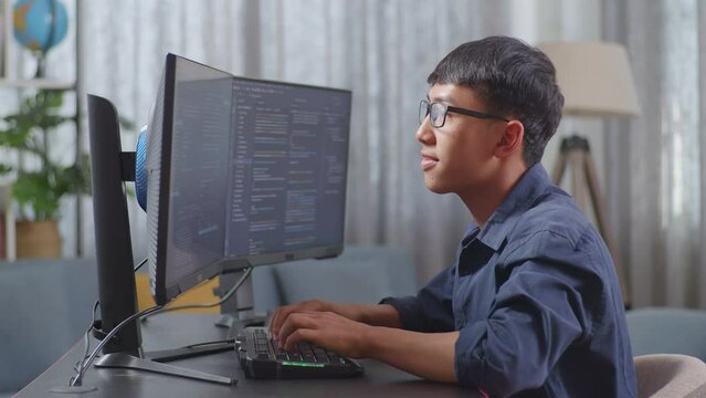 Asian Boy Programmer Creating Innovative Software Engineer Developing App, Program, Video Game On Desktop Computer At Home. Terminal With Coding Language 
