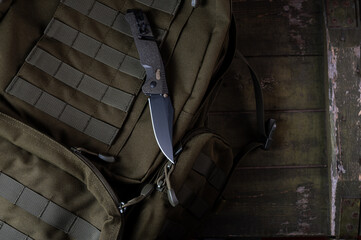 Obraz premium Folding sharp army knife on a military backpack. Knife with clip and safety. Backpack with molle ribbons. Military composition.