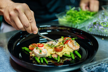 The chef finishes decorating the dish with kitchen tweezers. Omelet with shrimp, caviar and grilled tomatoes
