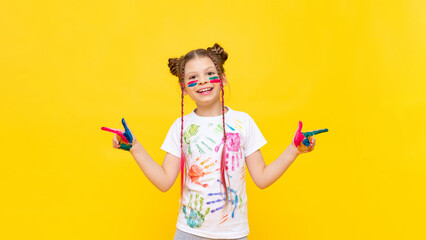 A beautiful little girl with stained hands in paint points her fingers in different directions. A child in paint on a yellow background.