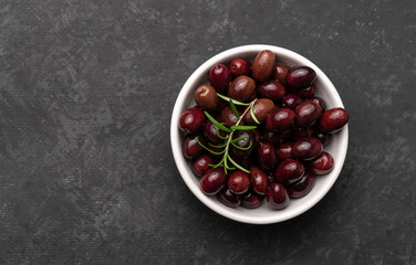 Bowl of tasty dark-purple olives on dark table. Flat lay with copy space