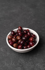 Bowl of tasty dark-purple olives on dark table with copy space