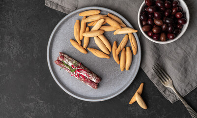 Plate with Spanish sticks of mini fuet and picos - bread sticks and bowl with dark olives on the...