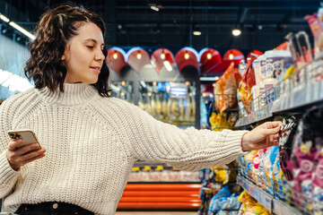 a woman chooses a product from a list of products on the phone in a supermarket