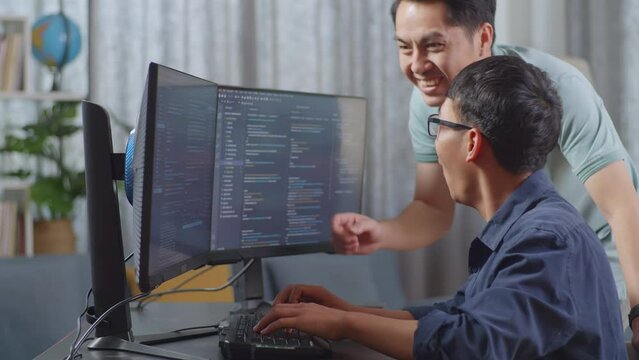 Happy Asian Boy And Male Celebrating Succeed Creating Software Engineer Developing App, Program, Video Game On Desktop Computer At Home. Terminal With Coding Language
