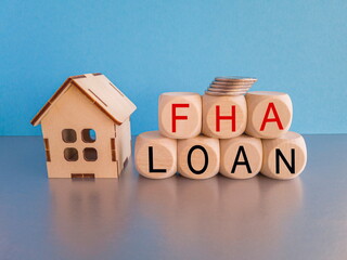 FHA federal housing administration loan symbol. Concept words 'FHA federal housing administration loan' on wooden cubes on a beautiful blue background. Model of house. Business and FHA loan concept. 