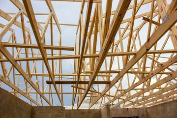 Wooden frame of a lattice of roof beams on a building under construction without any roof tiles placed on it. 
