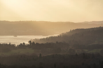 Stunning Winter sunrise landscape view from Loughrigg Fell across towards Windermere with stunning sun beams coming from the dark clouds above