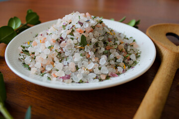 colorful mountain herb salt on a white plate on a dark wooden plate with a heart kitchen spoon on a dark wooden background