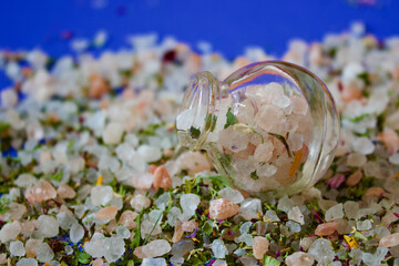 small salt shaker filled with herbal salt on a pile of herbal salt, blue background, close up