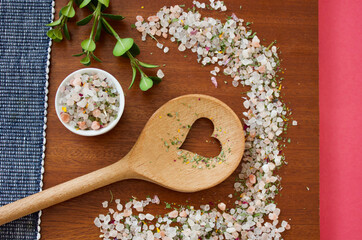 mountain herb salt in a small white container on a dark wooden plate with a heart kitchen spoon on a blue white and pink background, top view, copy space