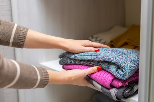 Woman Takes Warm Clothes Out Of The Closet. Clothes On The Shelf In The Closet