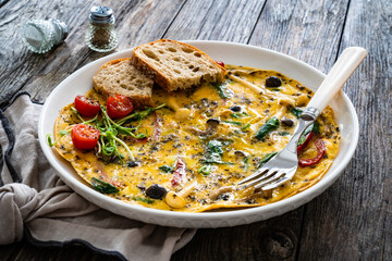 Delicious breakfast - scrambled eggs with onion, red pepper, shimeji mushrooms  and black olives on wooden table
