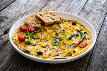 Delicious breakfast - scrambled eggs with onion, red pepper, shimeji mushrooms  and black olives on wooden table
