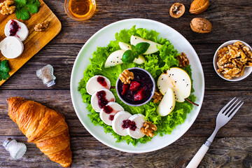 Fresh salad - goat cheese, pear, jam, lettuce and walnuts on wooden background

