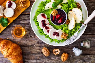 Fresh salad - goat cheese, pear, jam, lettuce and walnuts on wooden background

