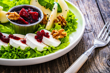 Fresh salad - goat cheese, pear, jam, lettuce and walnuts on wooden background

