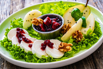 Fresh salad - goat cheese, pear, jam, lettuce and walnuts on wooden background

