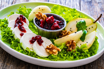 Fresh salad - goat cheese, pear, jam, lettuce and walnuts on wooden background

