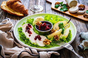 Fresh salad - goat cheese, pear, jam, lettuce and walnuts on wooden background

