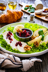 Fresh salad - goat cheese, pear, jam, lettuce and walnuts on wooden background

