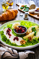 Fresh salad - goat cheese, pear, jam, lettuce and walnuts on wooden background

