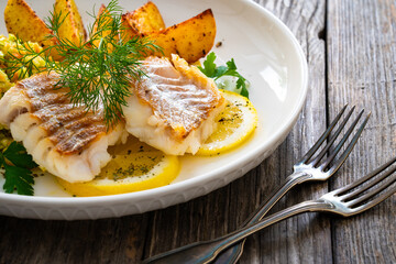 Fish dish - fried cod with baked potatoes and fresh vegetables on wooden table
