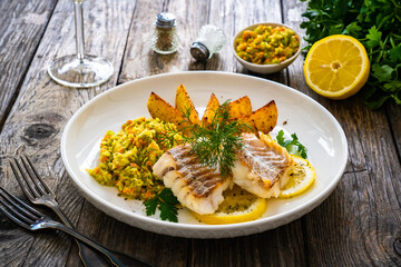 Fish dish - fried cod with baked potatoes and fresh vegetables on wooden table
