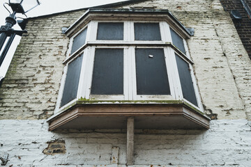 Grungy view of a boarded up bay window shown on a derelict town home. Used by squatters and drug...