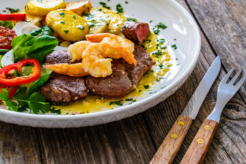 Fried beef sirloin steak with fried garlic prawns on and  potatoes on wooden table
