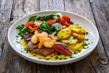 Fried beef sirloin steak with fried garlic prawns on and  potatoes on wooden table
