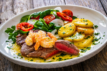 Fried beef sirloin steak with fried garlic prawns on and  potatoes on wooden table
