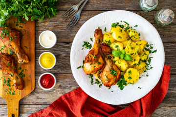BBQ chicken drumsticks with fried potatoes, lettuce and ketchup on wooden table
