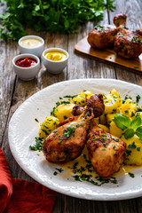 BBQ chicken drumsticks with fried potatoes, lettuce and ketchup on wooden table
