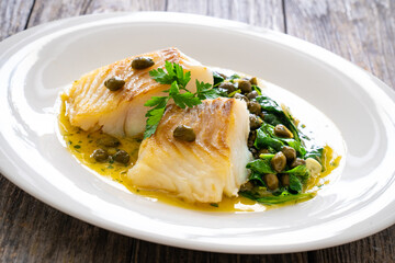 Fish dish - fried cod with spinach and capers in saffron sauce on wooden table
