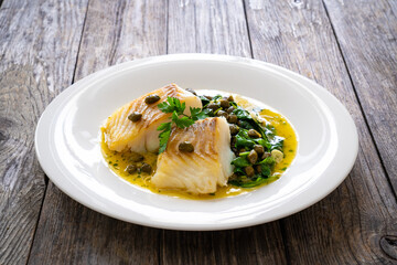 Fish dish - fried cod with spinach and capers in saffron sauce on wooden table
