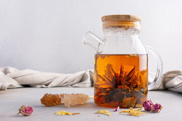 Glass teapot of hot fragrant craft blossom tea with dry rose bud and sugar