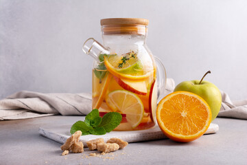 Glass teapot of hot healthy sweet fruit tea with fresh ripe citrus, apples, mint and thyme