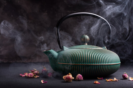 Hot green japanese cast iron teapot with steam and dry roses for tea break