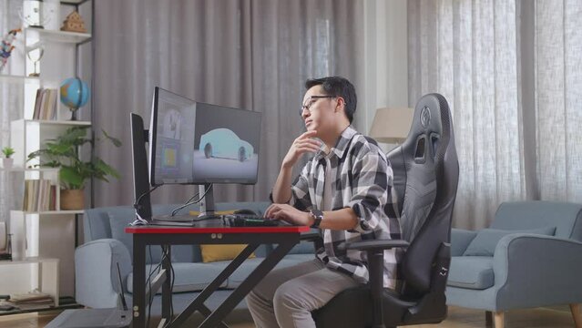 Side View Of Asian Male Automotive Designer Thinking Of Idea Then Raising His Index Finger While Working On 3D Model Of Ev Car On The Desktop Computers At Home
